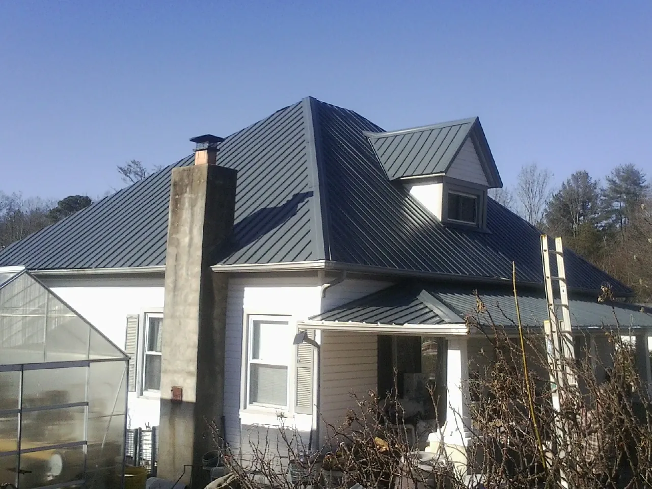 Dark blue standing seam metal roof on a white farmhouse with dormer — Slate & Tile Roof Repair by Roofing Brothers in Scio