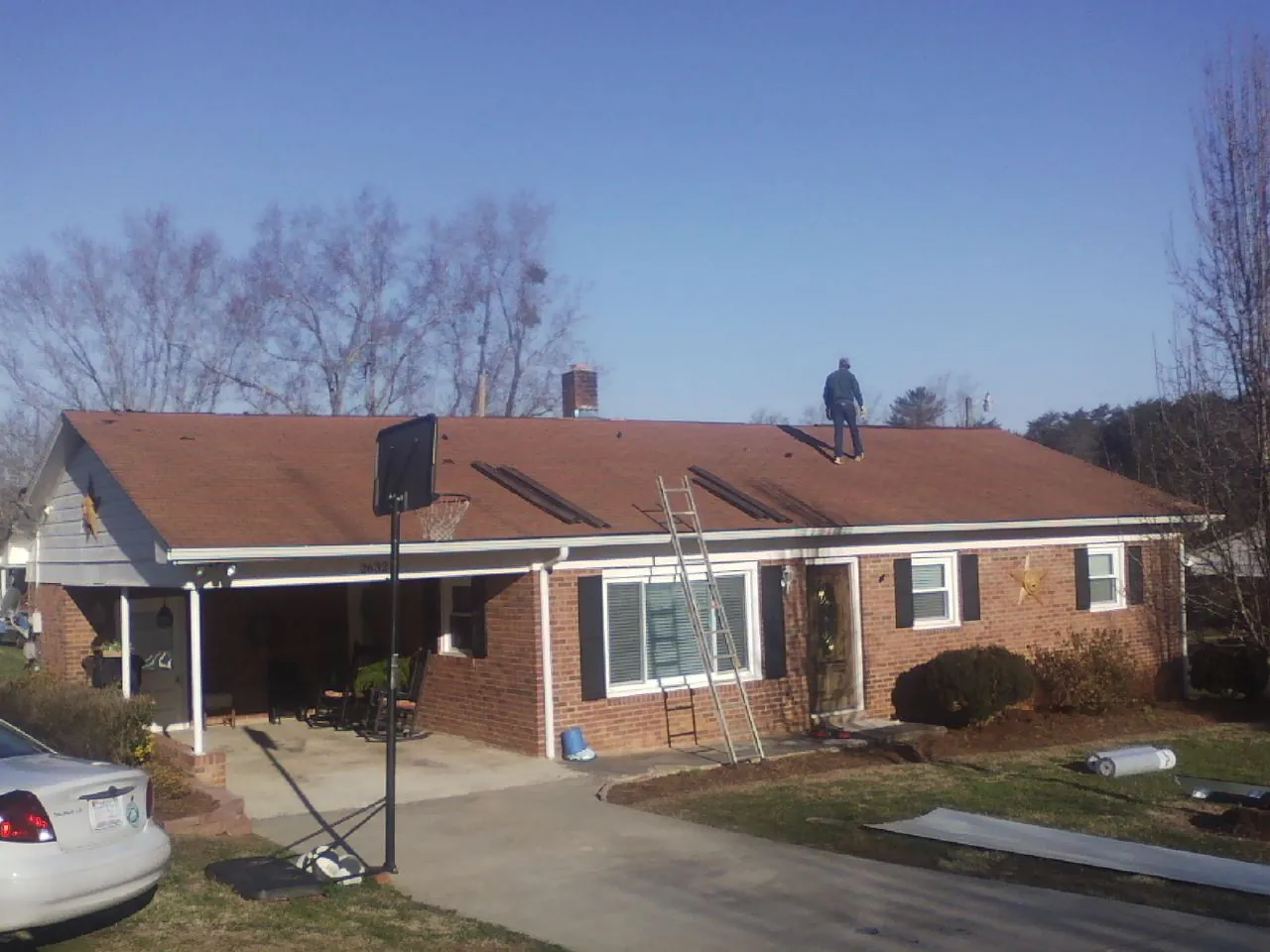 Roofer stripping a shingle roof on a brick ranch before metal panels in Scio