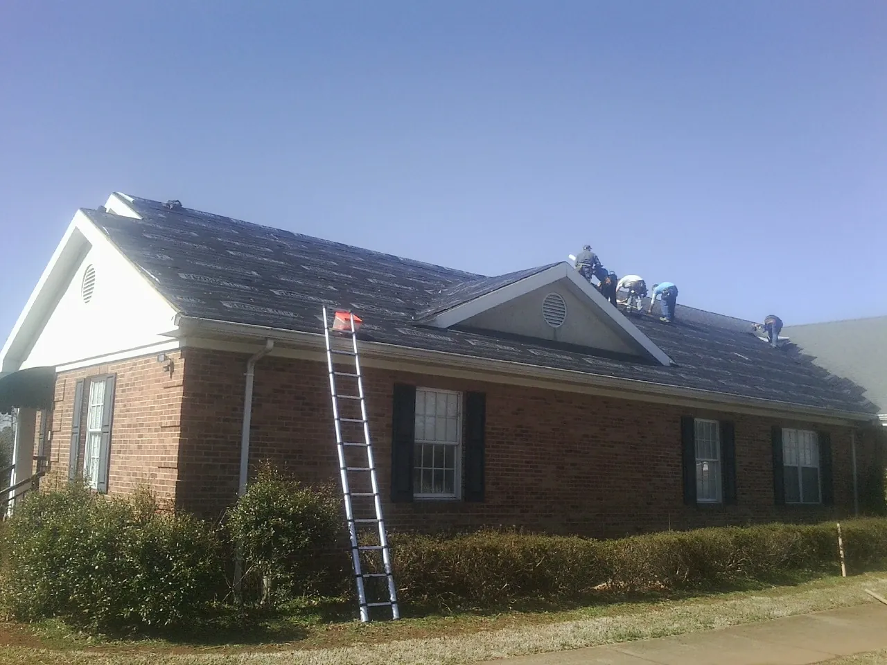 Crew tearing shingles off a brick ranch roof with a ladder set — Metal Roof Repair work by our crew in Scio