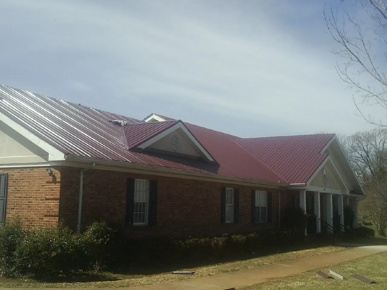Red metal roof with gabled entries on a long brick building, from a Hail Damage Roof Repair job in Scio