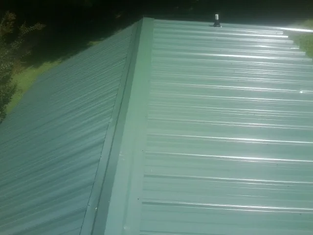 New green metal panels meeting at the ridge of a roof — Flat Roof Repair work by our crew in Scio