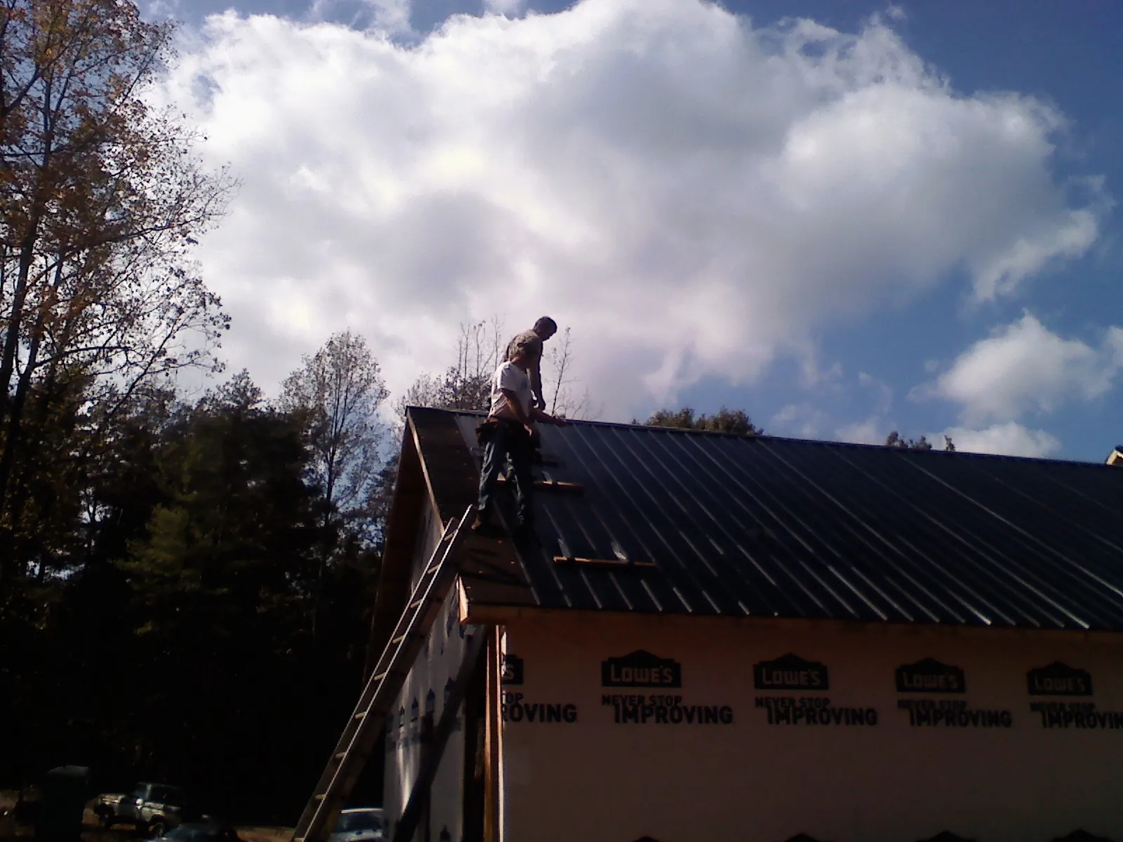 Roofer fastening dark metal panels high against a cloudy sky, from a Roof Inspection job in Scio
